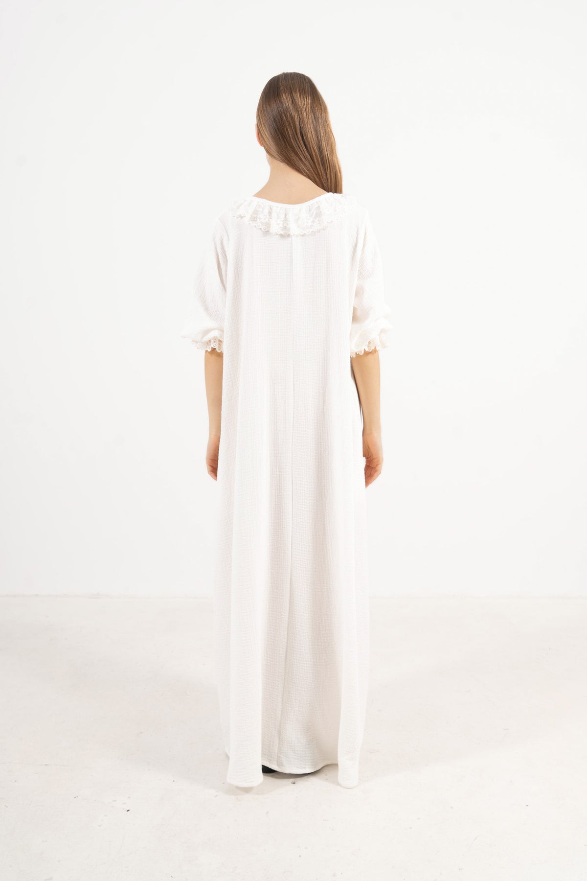 The refined back view of the MOCHA Aérienne long dress in fine soft cotton, displaying a clean, understated silhouette laid flat on a polished white floor.