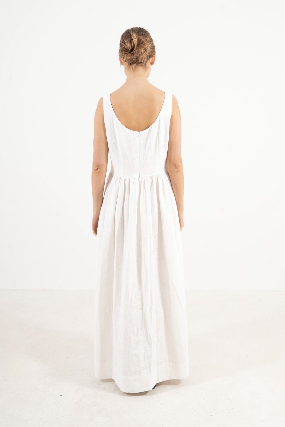 The refined back view of the MOCHA Amandine long dress in cotton and ramie, displaying a clean, understated silhouette laid flat on a polished white floor.