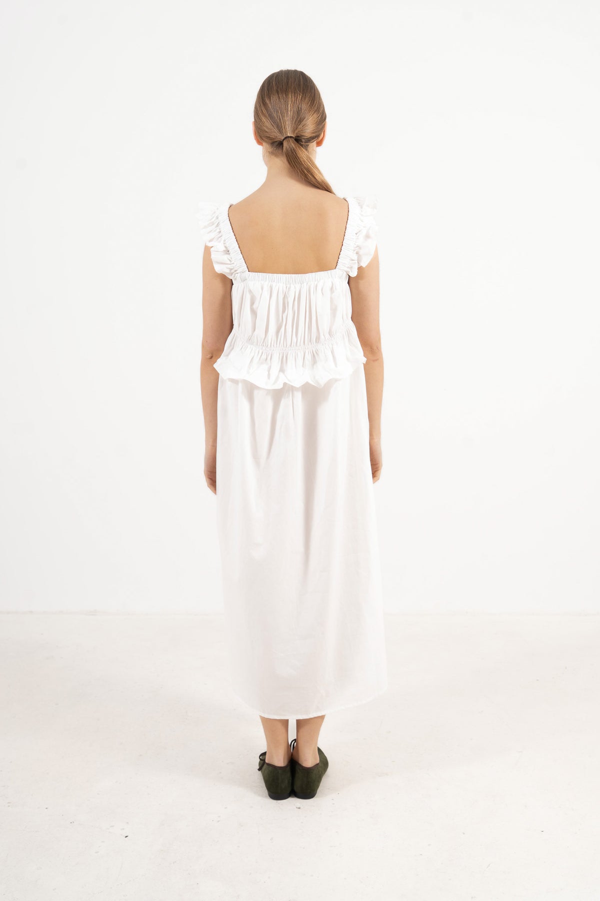 The refined back view of the MOCHA Chloé long dress in fine organic cotton, displaying a clean, timeless silhouette laid flat on a polished white floor.