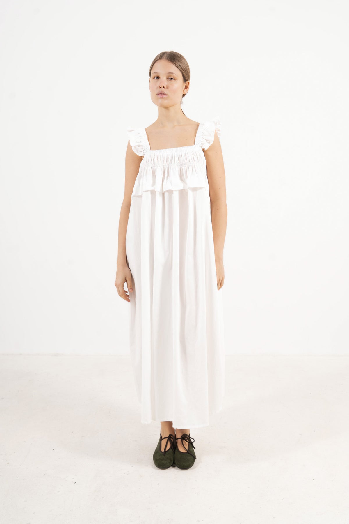 A sophisticated profile view of the standalone MOCHA Chloé dress in pure organic cotton, revealing its graceful design lines resting on a clean white surface.