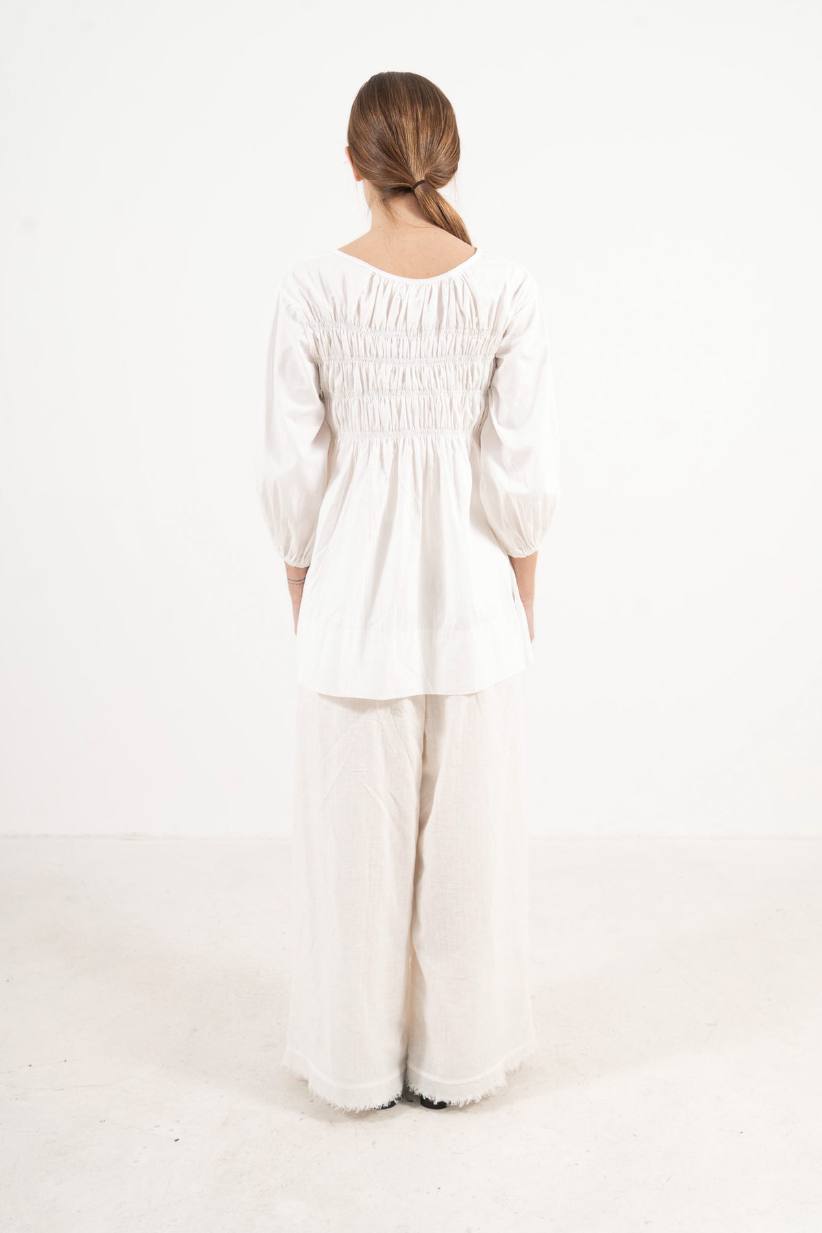 Back view of the timeless organic cotton blouse on a model, capturing the elegant heritage, calm ease, and seamless tailoring of the piece.