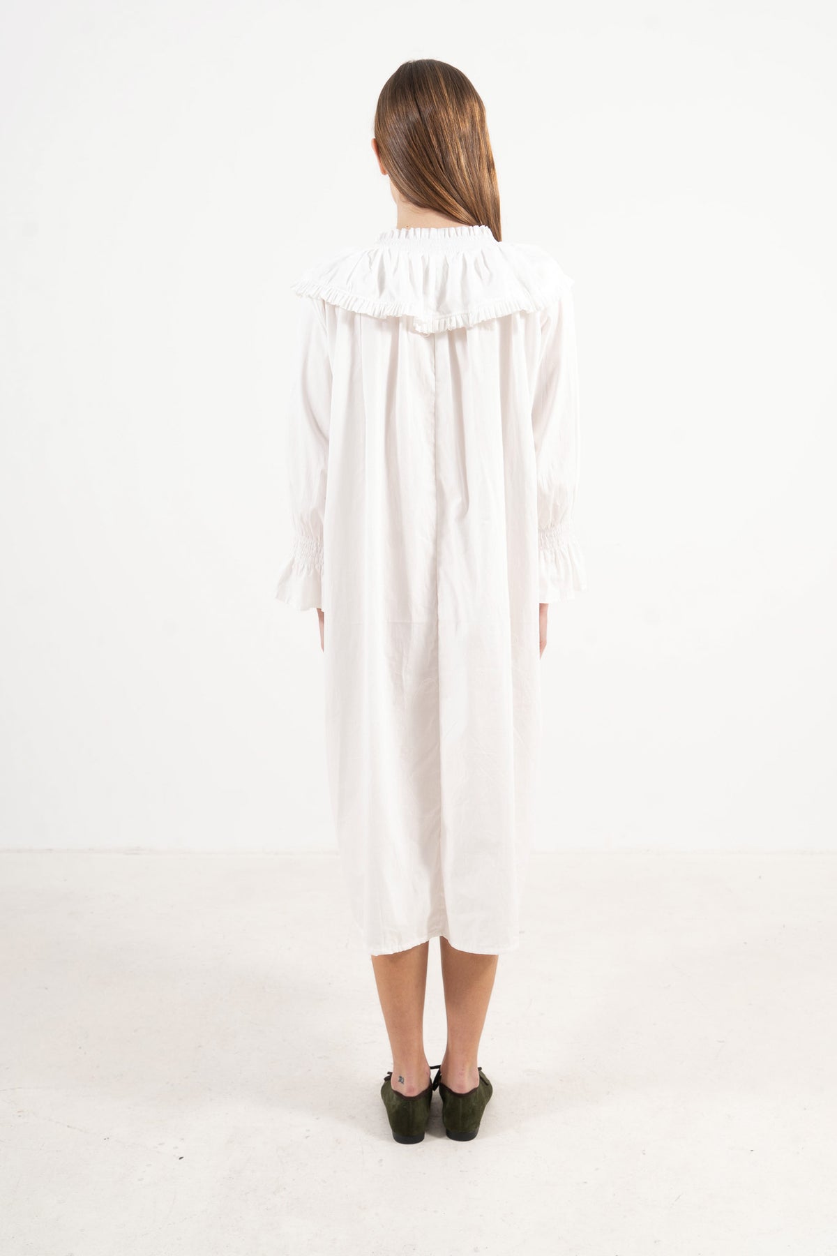 Back view of the timeless long cotton dress on a model, illustrating a softly elevated look and the understated opulence of its tailoring.