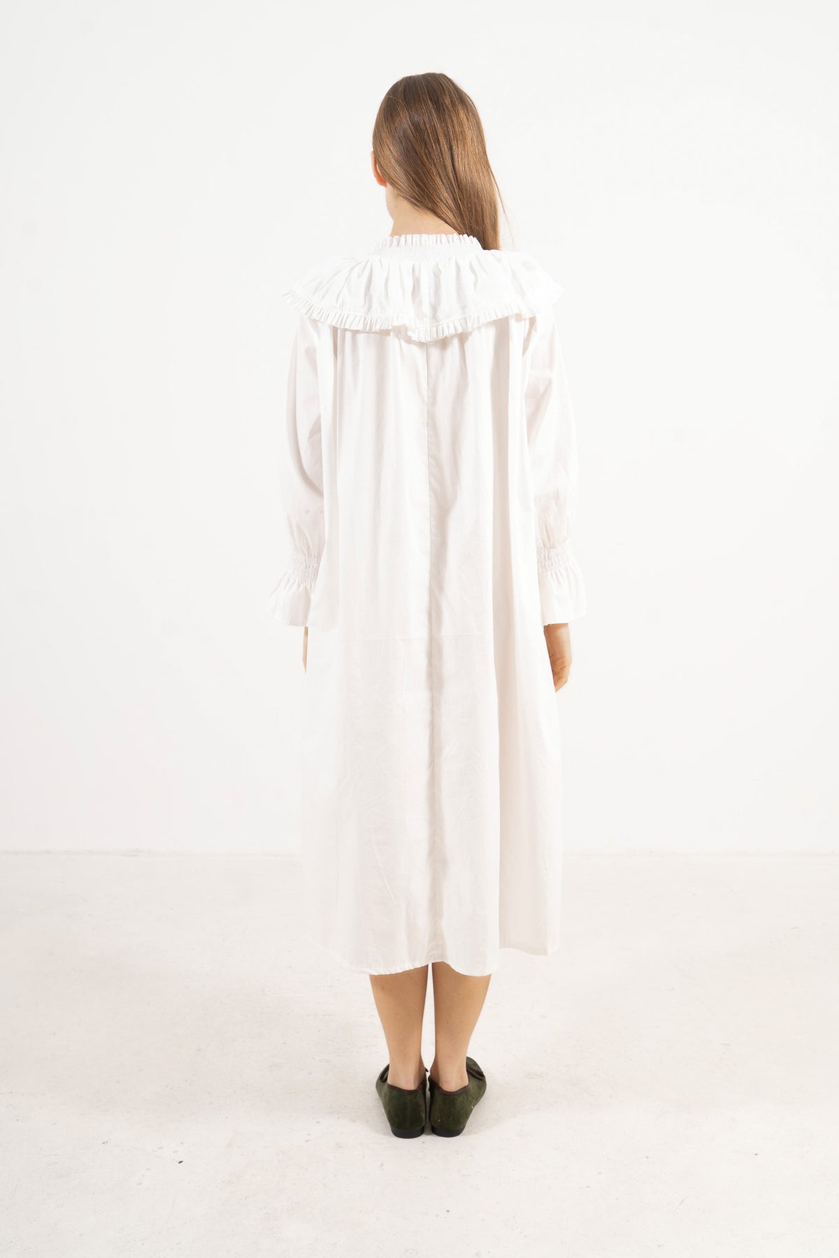 Back view of the timeless long cotton dress on a model, illustrating a softly elevated look and the understated opulence of its tailoring.