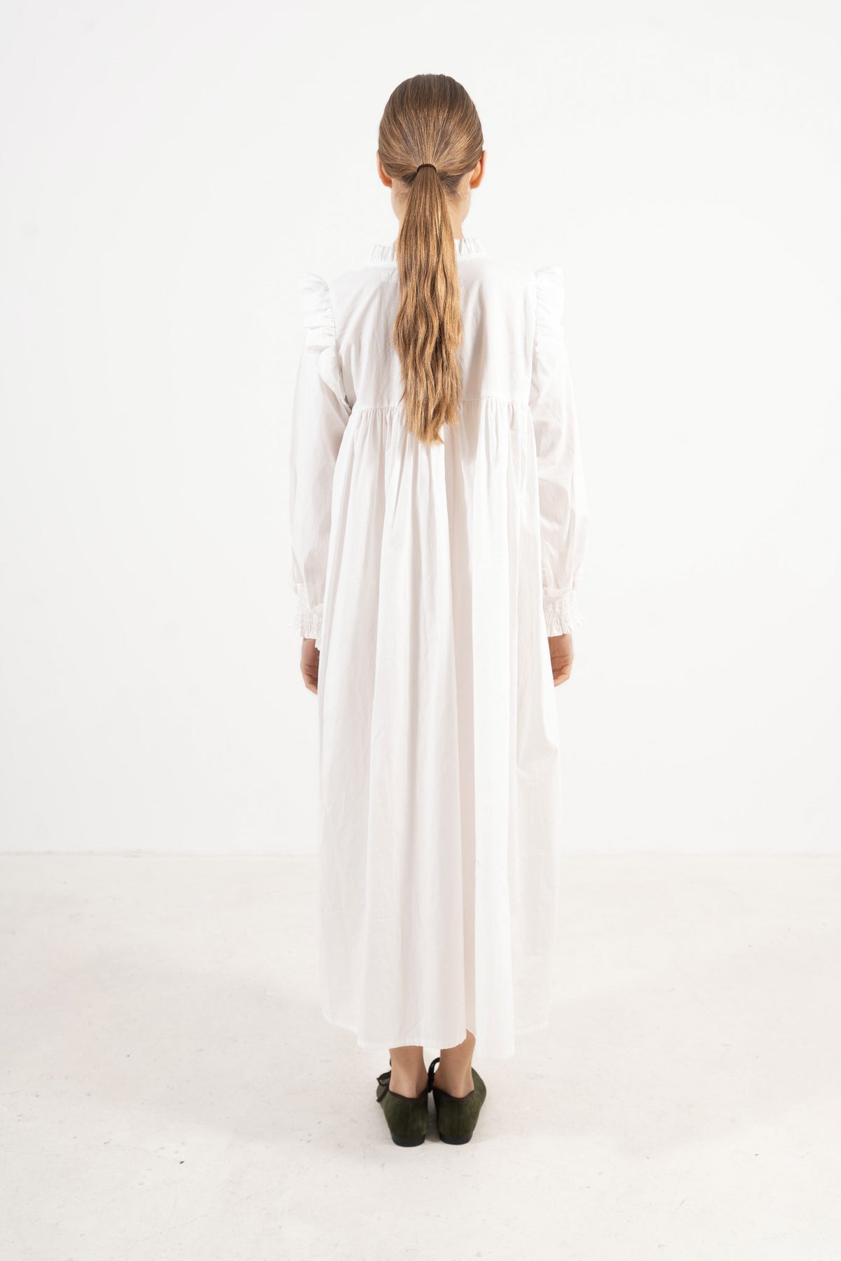 Back view of the timeless long cotton dress on a model, illustrating a softly elevated look and the understated opulence of its tailoring.