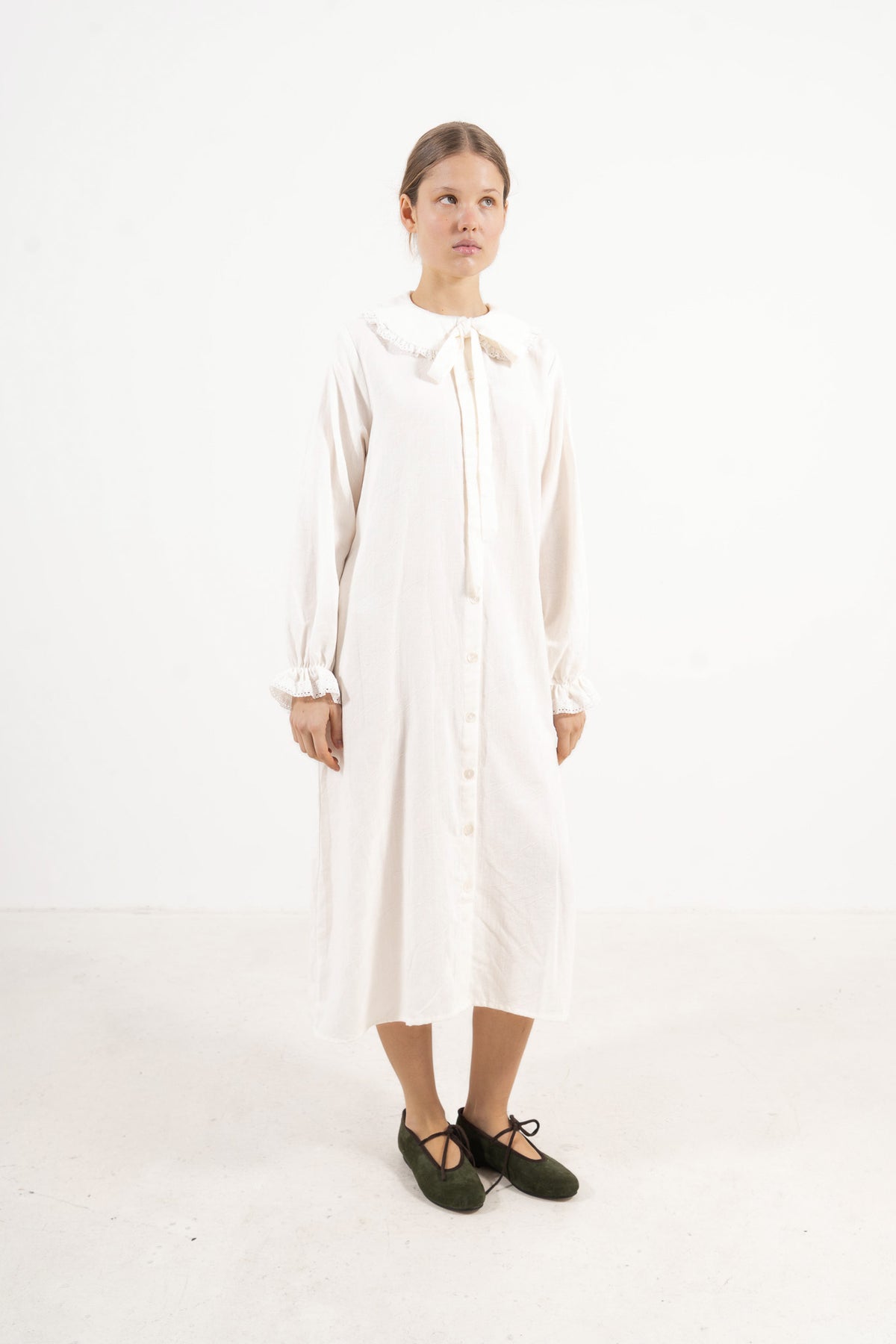 Side profile capture of the white organic cotton dress, emphasizing the flowing movement and airy lightness signature to the collection.
