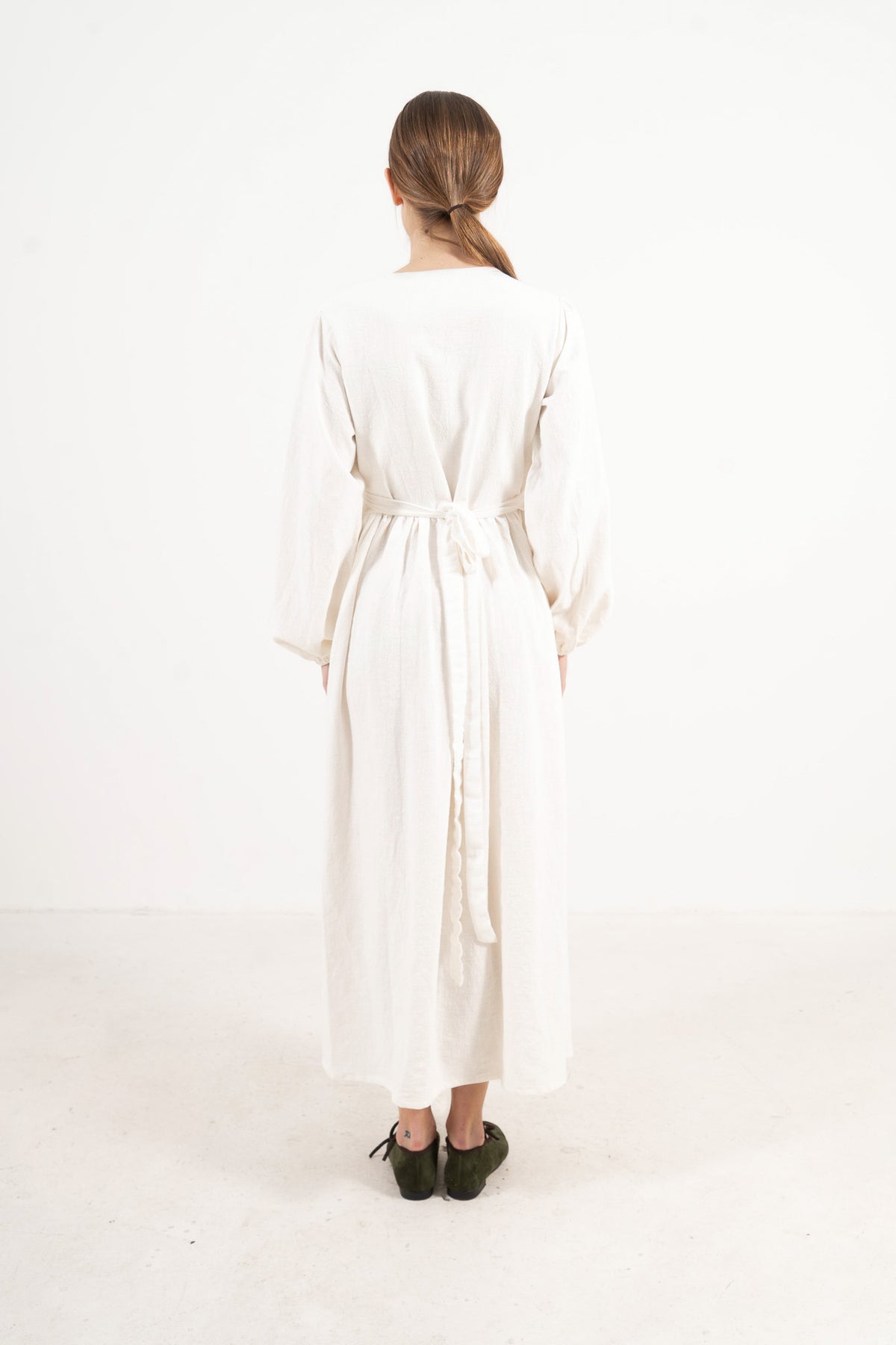 Back view of the long apron on a model, showcasing the delicate tie straps and the fine craftsmanship of the piece