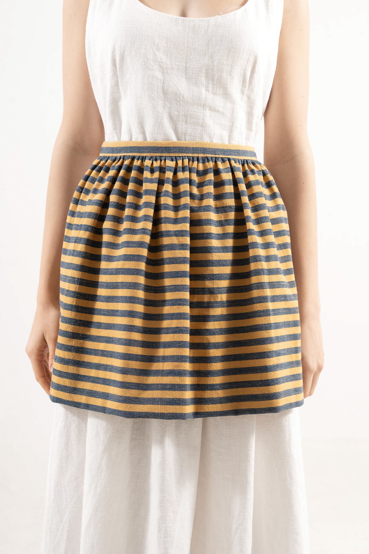 Close-up detail shot focusing on the delicate volants, fine stripe pattern, and premium cotton weave, celebrating the beauty of slow kitchen rituals.