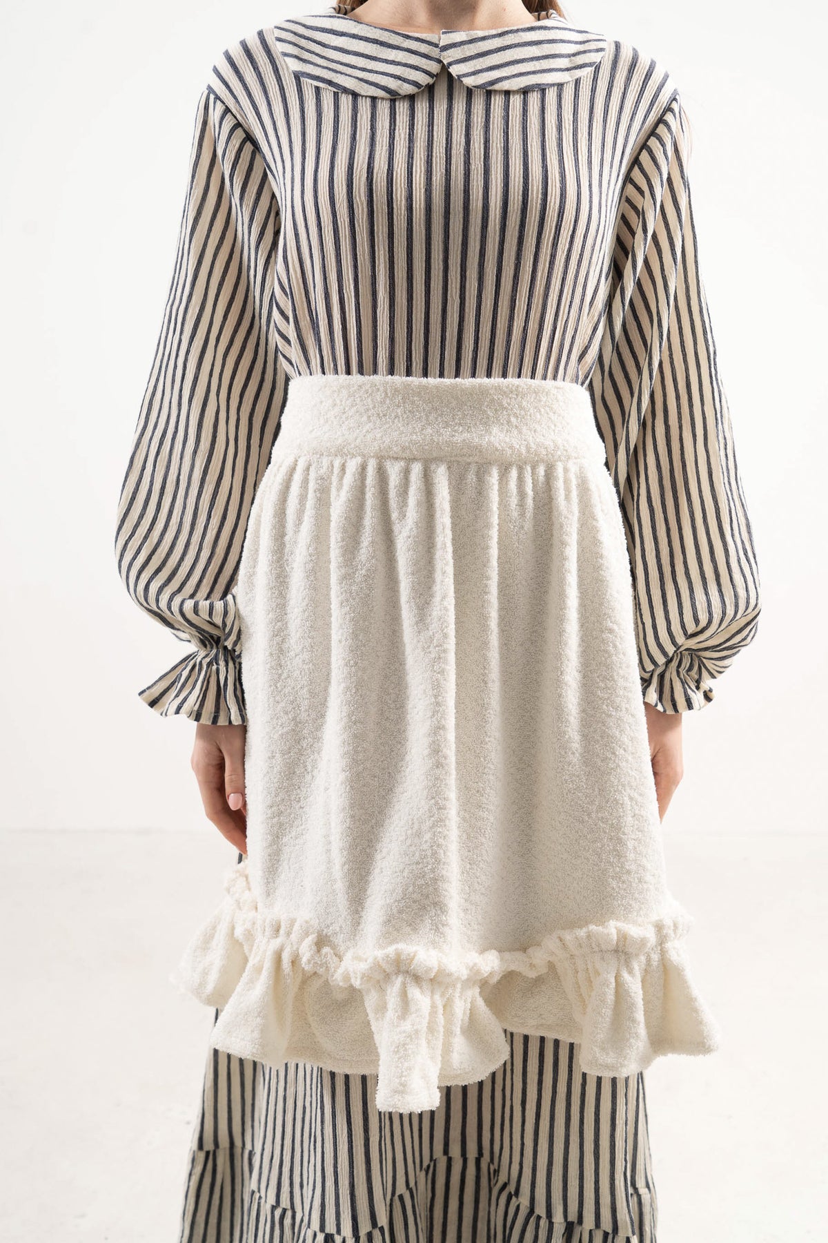 Close-up detail shot focusing on the delicate volants and premium cotton weave, celebrating the beauty of slow kitchen rituals.