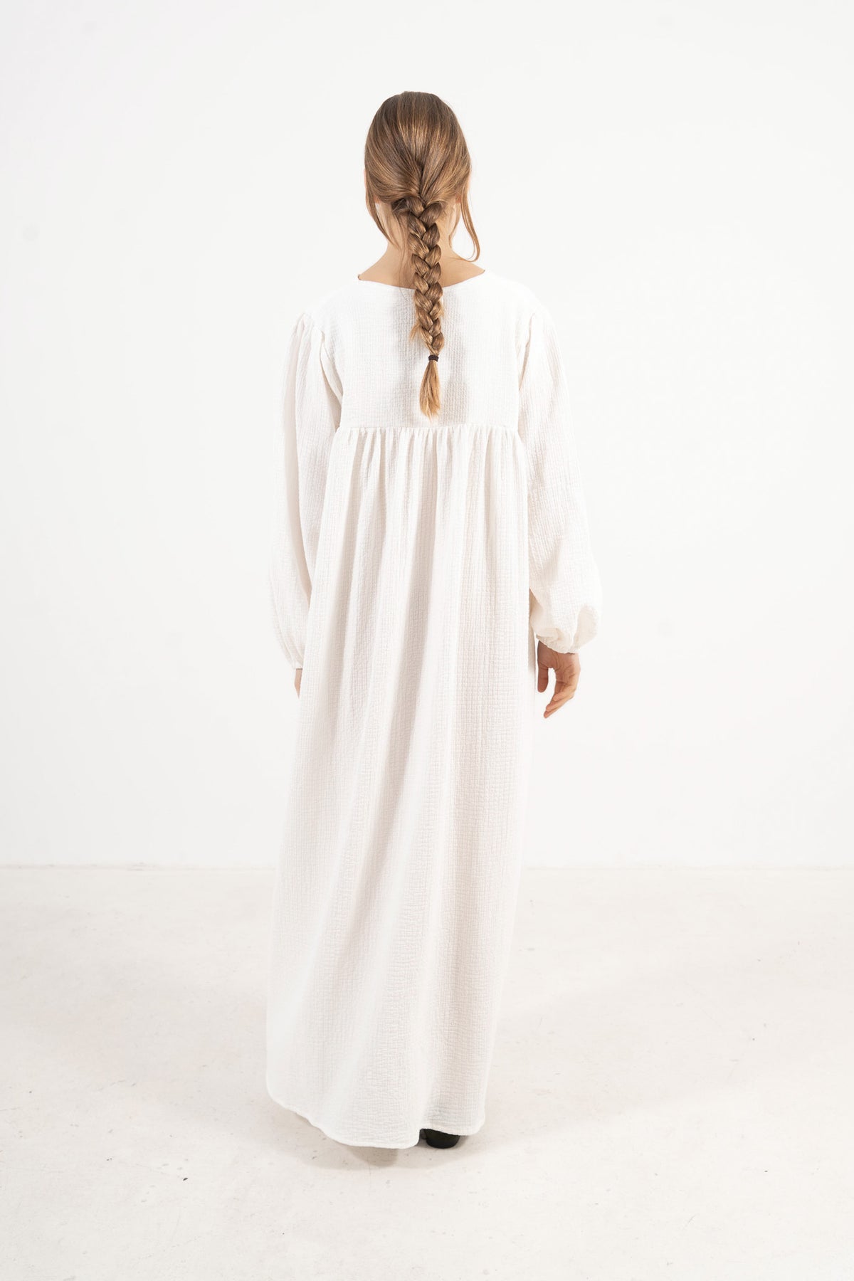 The refined back view of the MOCHA Pearl Bow dress in exquisite organic cotton, displaying a clean, timeless silhouette laid flat on a polished white floor.