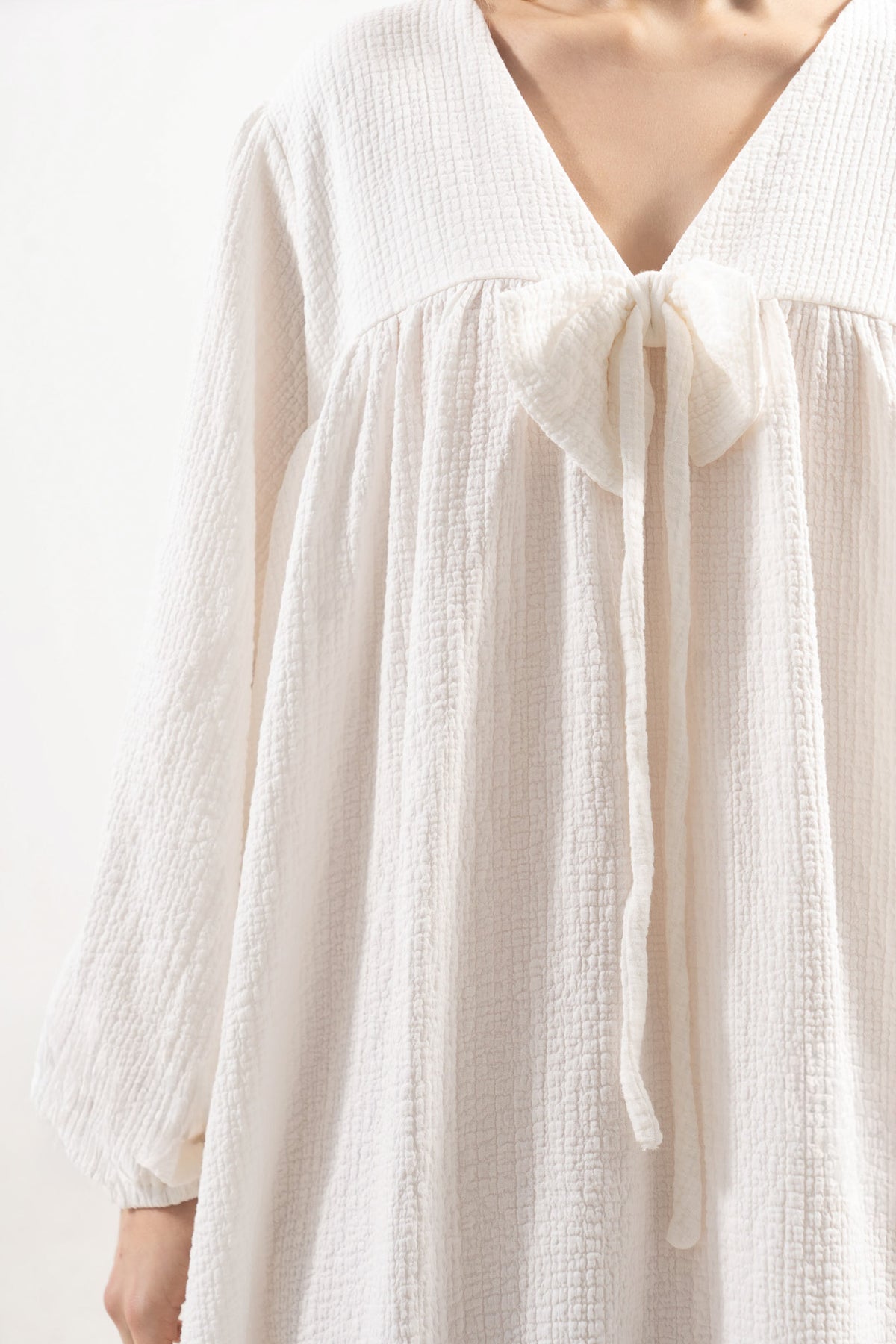 An exquisite close-up detail of the MOCHA Pearl Bow dress, capturing the delicate craftsmanship of its feminine bows and the soft, premium weave of its fine cotton fabric.