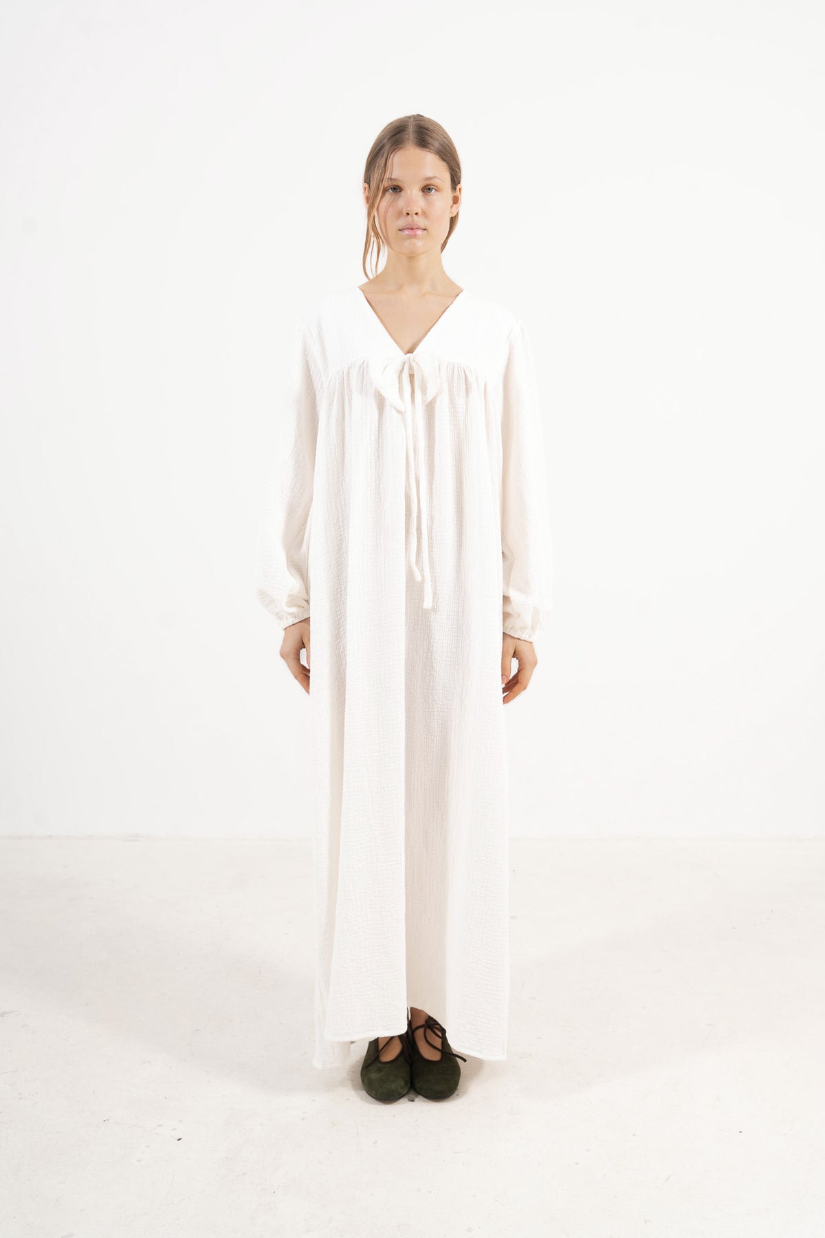 An elegant front view of the MOCHA Pearl Bow dress, meticulously crafted from the finest organic cotton and draped beautifully upon a pristine white floor.