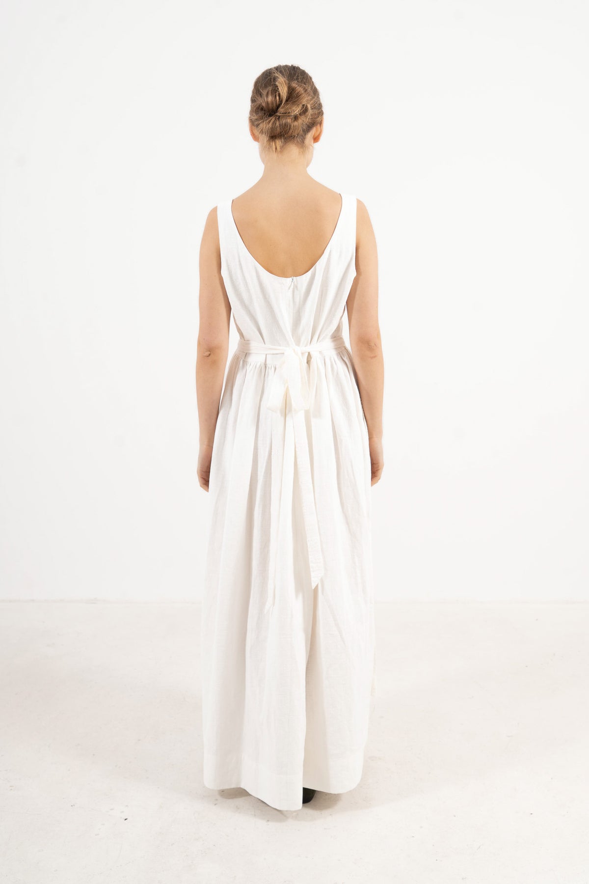 Back view of Le Tablier Long Apron by MOCHA, highlighting the elegant rear drape, crossed straps, and refined tie closure details.