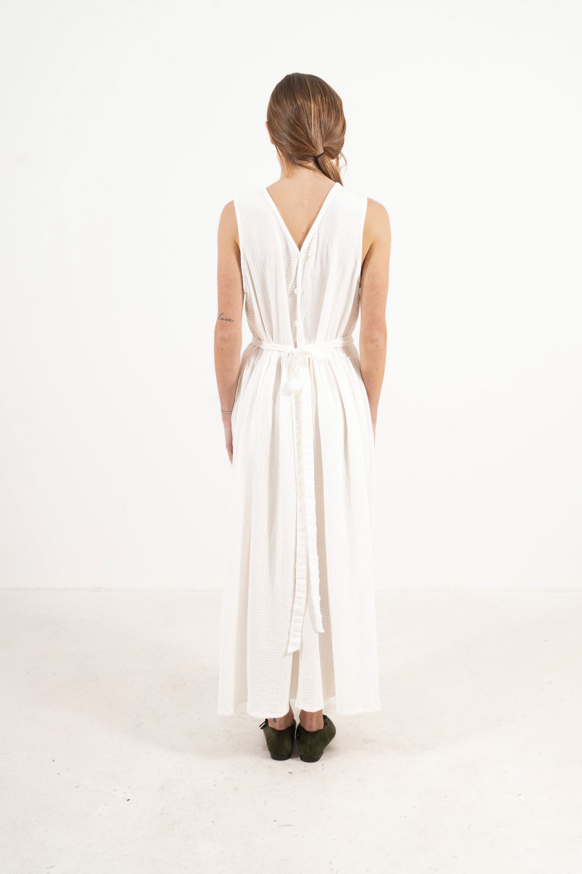 Back view of Le Tablier Mid Apron by MOCHA, showcasing the mid-length rear drape, crossed tie straps, and refined closure layout.