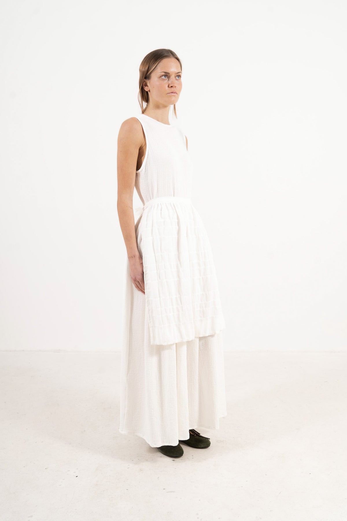 Side profile view of Le Tablier Mid Apron by MOCHA, capturing the delicate flow of the shoulder volants and the clean drape of the mid-length silhouette.